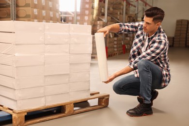 Worker wrapping boxes in stretch film at warehouse