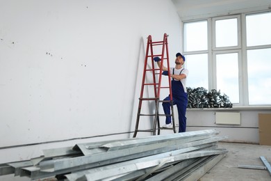 Construction worker climbing up stepladder in room prepared for renovation