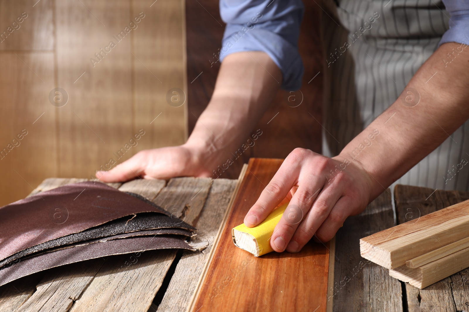 Photo of Man polishing wooden plank with sandpaper at table indoors, closeup