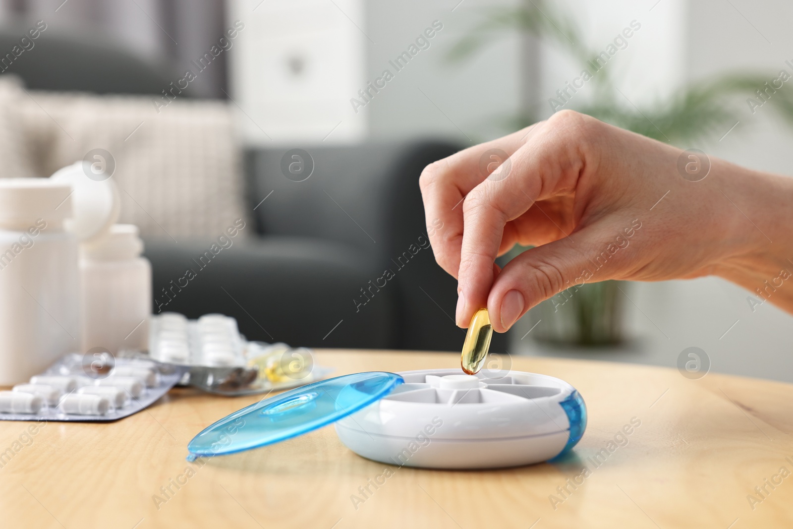 Photo of Woman with pills and organizer at light wooden table, closeup