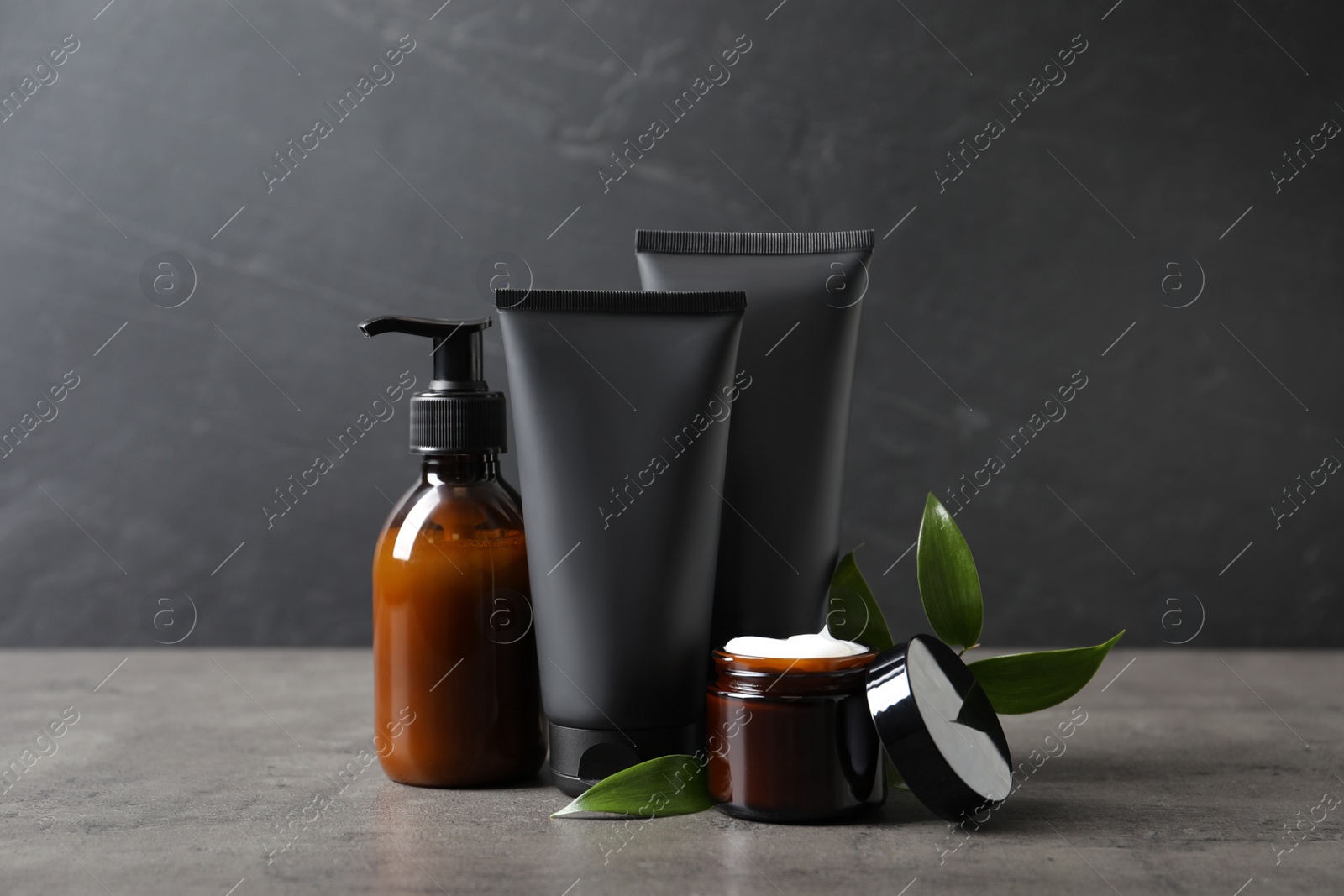 Photo of Facial cream and other men's cosmetic with green leaves on grey stone table. Mockup for design