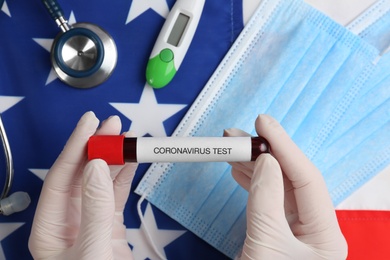Photo of Scientist holding test tube with blood sample over American flag, closeup. Coronavirus pandemic in USA
