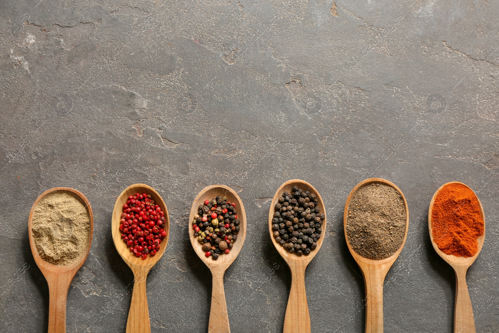 Photo of Spoons with different types of pepper and space for text on gray background