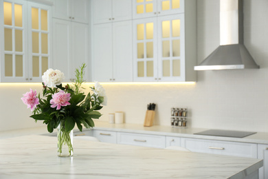 Photo of Peony bouquet on white marble table in kitchen interior