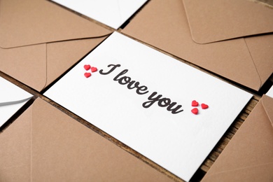 Photo of Sheet of paper with phrase I Love You, envelopes and heart shaped sprinkles on wooden table, closeup
