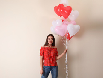 Photo of Beautiful young woman with heart shaped balloons on beige background, space for text. Valentine's day celebration
