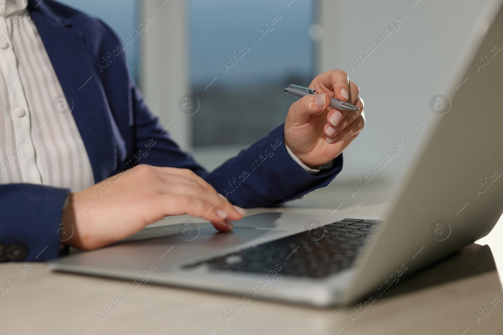 Photo of Woman with pen working on laptop at wooden table, closeup. Electronic document management