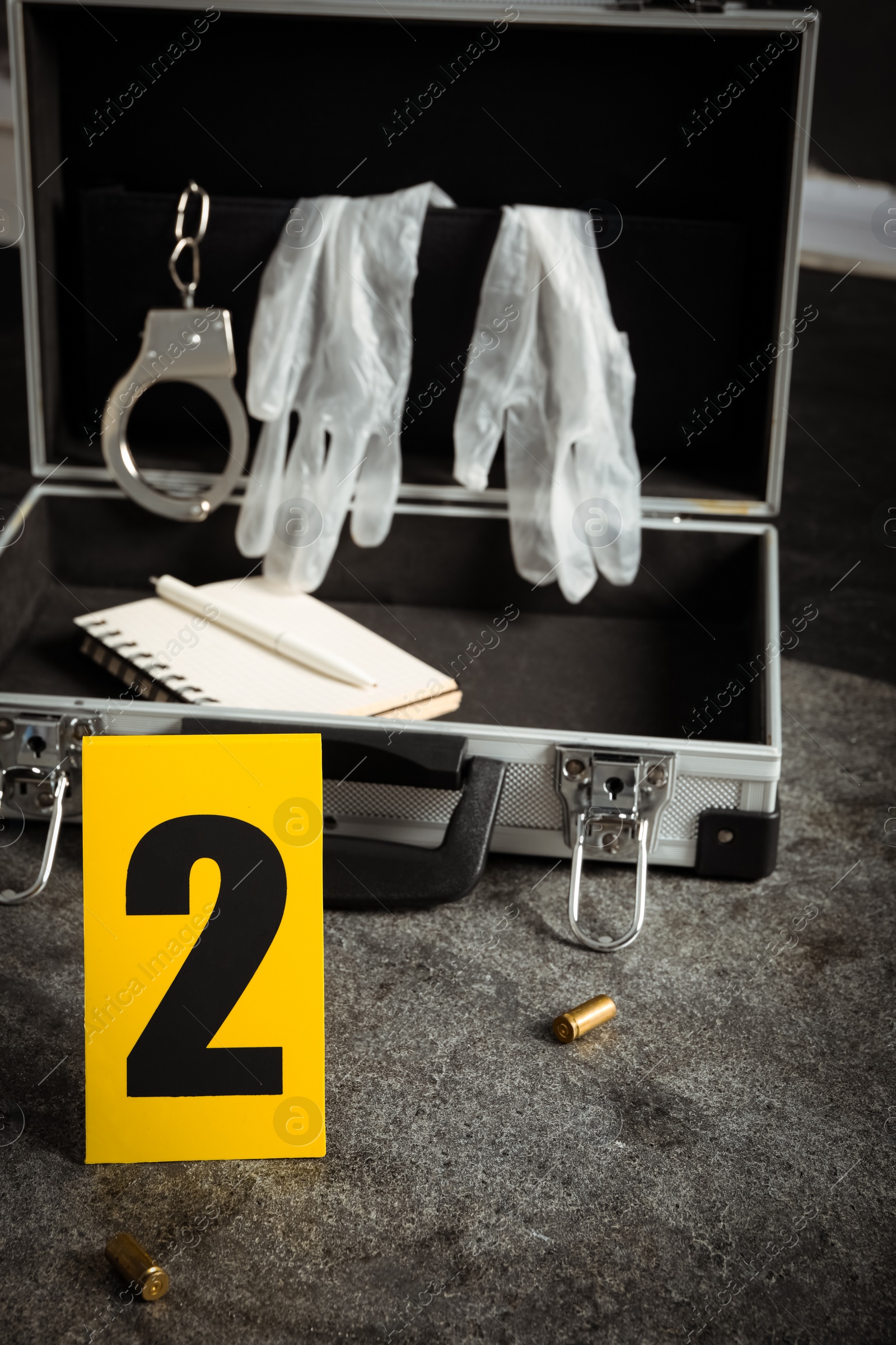 Photo of Crime scene marker and open case with police equipment on grey stone table