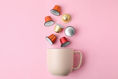 Many coffee capsules and cup on pink background, top view