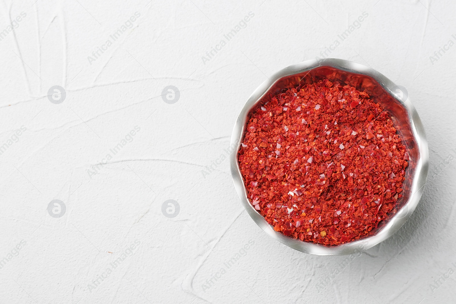 Photo of Bowl with chili pepper flakes on light background, top view