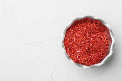 Photo of Bowl with chili pepper flakes on light background, top view