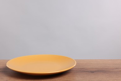 Empty ceramic plate on wooden table against light background, space for text