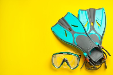 Pair of turquoise flippers and mask on yellow background, flat lay. Space for text