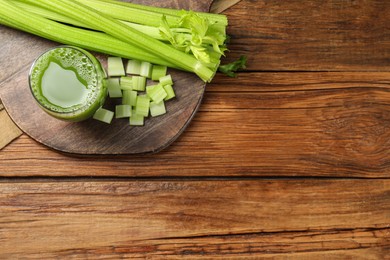 Glass of celery juice and fresh vegetables on wooden table, top view. Space for text