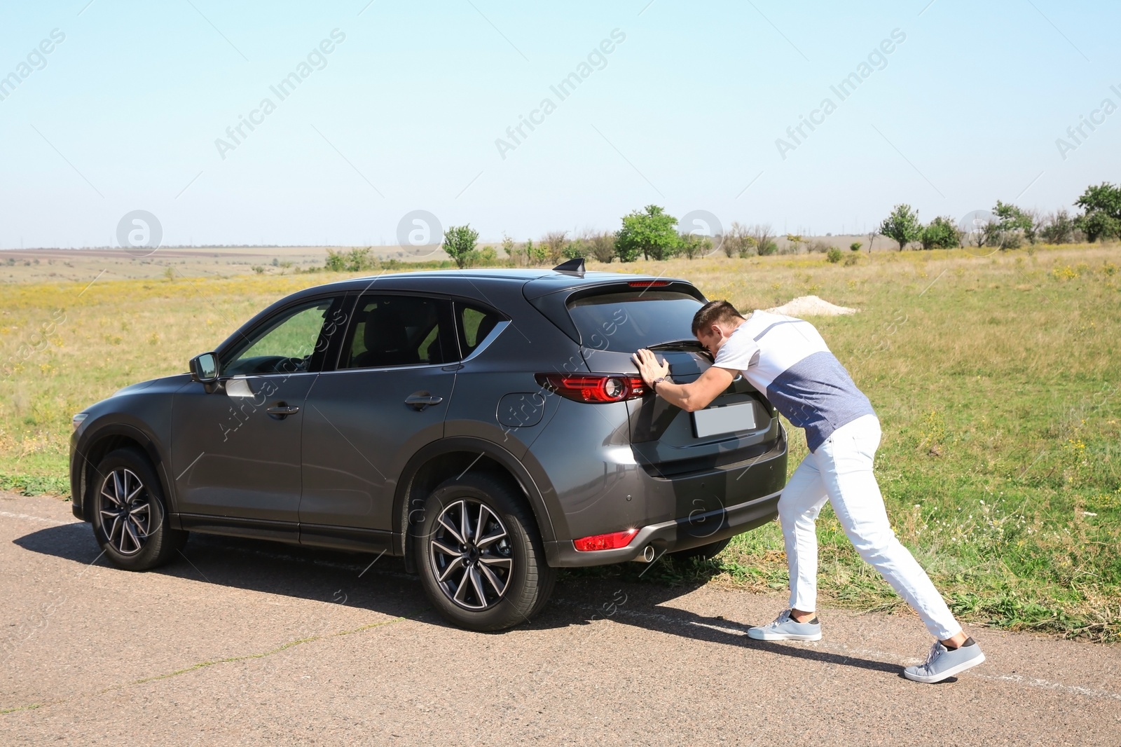 Photo of Man pushing broken car along country road