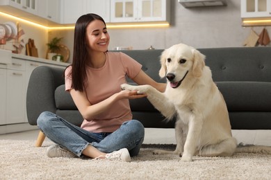 Photo of Cute Labrador Retriever dog giving paw to happy woman on floor at home. Adorable pet