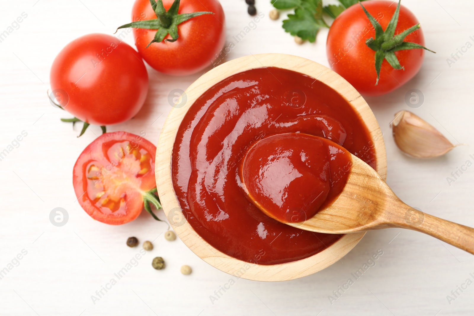 Photo of Taking delicious tomato ketchup with spoon from bowl at white table, top view