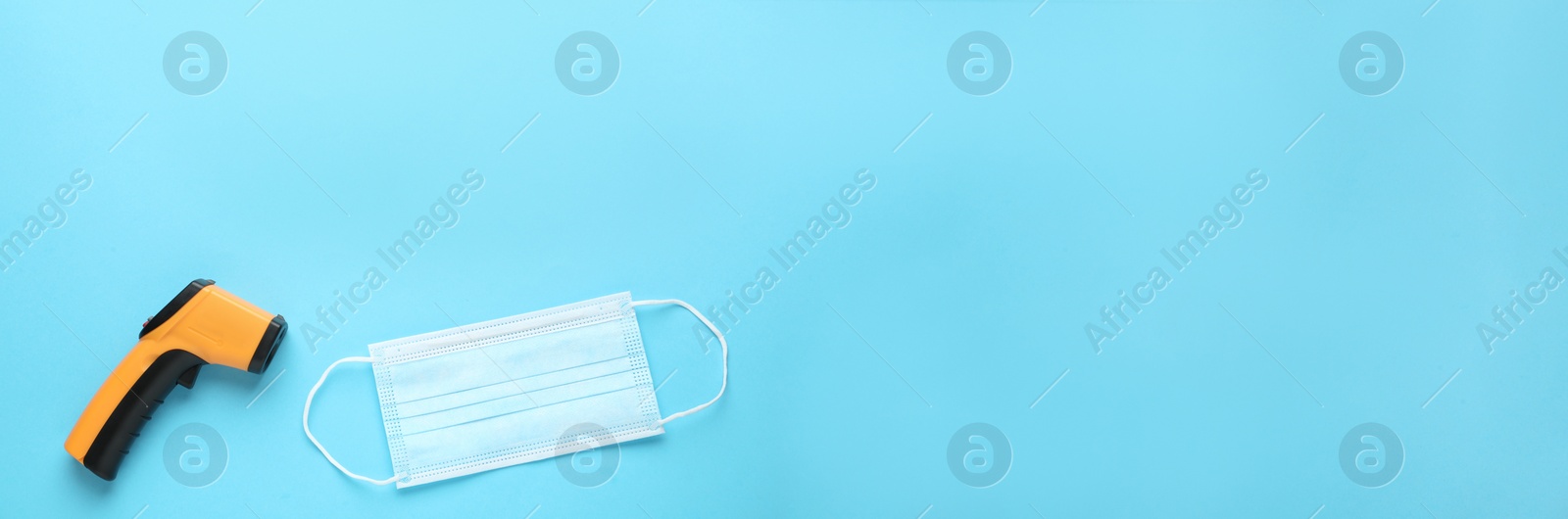 Photo of Infrared thermometer and medical mask on light blue background, flat lay with space for text. Checking temperature during Covid-19 pandemic