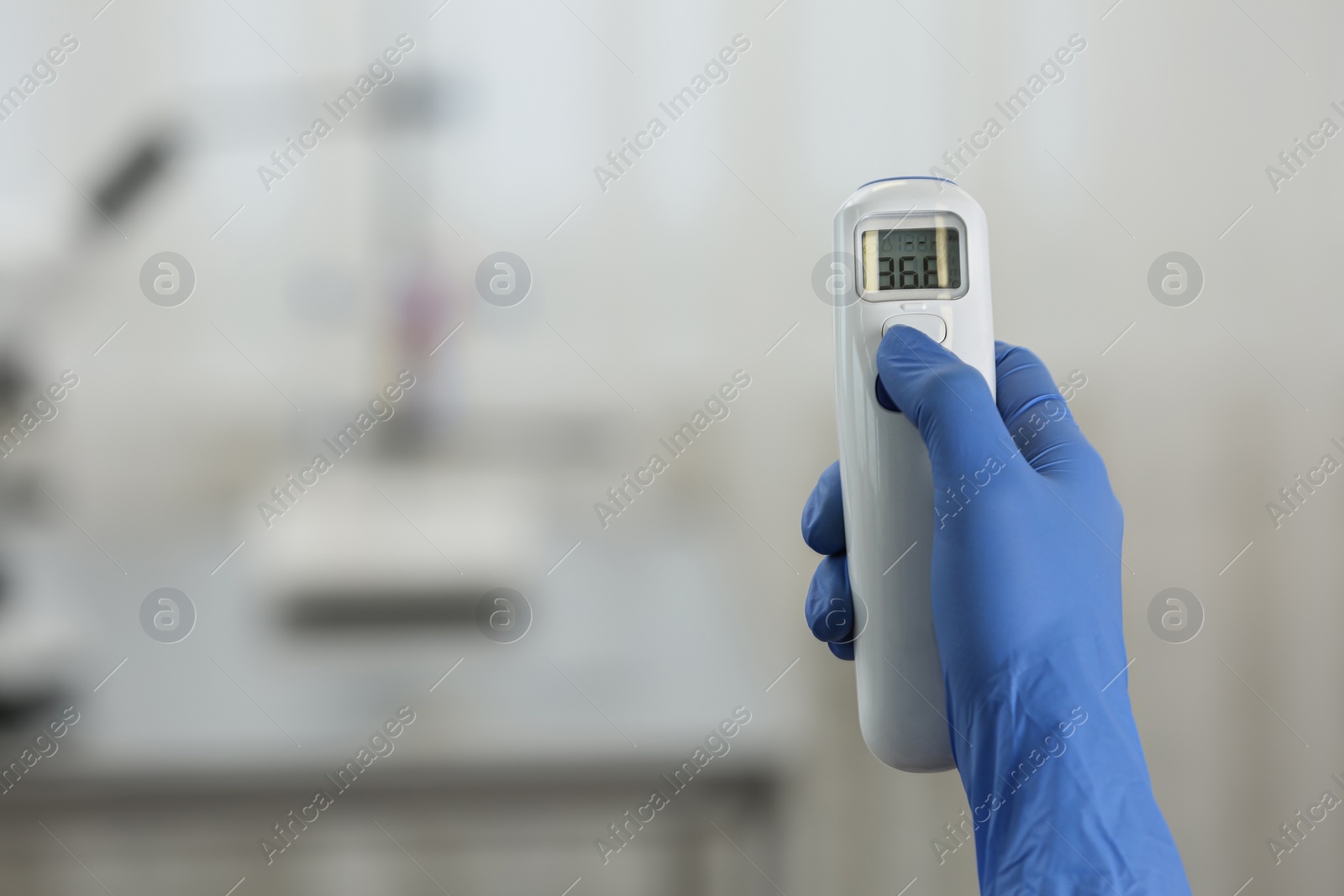 Photo of Closeup view of doctor with infrared thermometer on blurred background, space for text. Checking temperature during Covid-19 pandemic