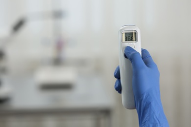 Closeup view of doctor with infrared thermometer on blurred background, space for text. Checking temperature during Covid-19 pandemic