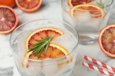 Photo of Delicious refreshing drink with sicilian orange and rosemary on white marble table, closeup