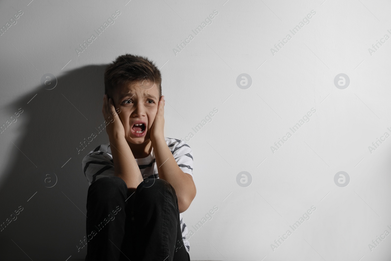 Photo of Scared little boy closing his ears near white wall, space for text. Domestic violence concept