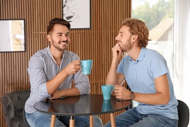 Photo of Happy gay couple with coffee at table indoors