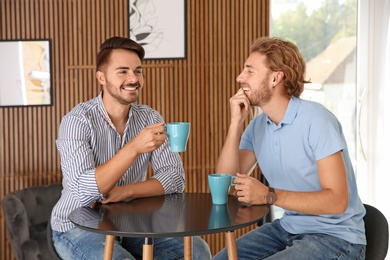 Happy gay couple with coffee at table indoors