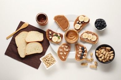 Photo of Toasts with different nut butters, banana slices, blueberries and nuts on white table, flat lay