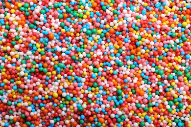 Photo of Bright colorful sprinkles as background, top view. Confectionery decor