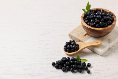 Photo of Ripe bilberries and leaves on white wooden table. Space for text