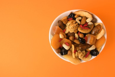 Photo of Bowl with mixed dried fruits and nuts on orange background, top view. Space for text