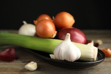 Photo of Plate with fresh onion bulbs, leek and garlic on wooden table, closeup