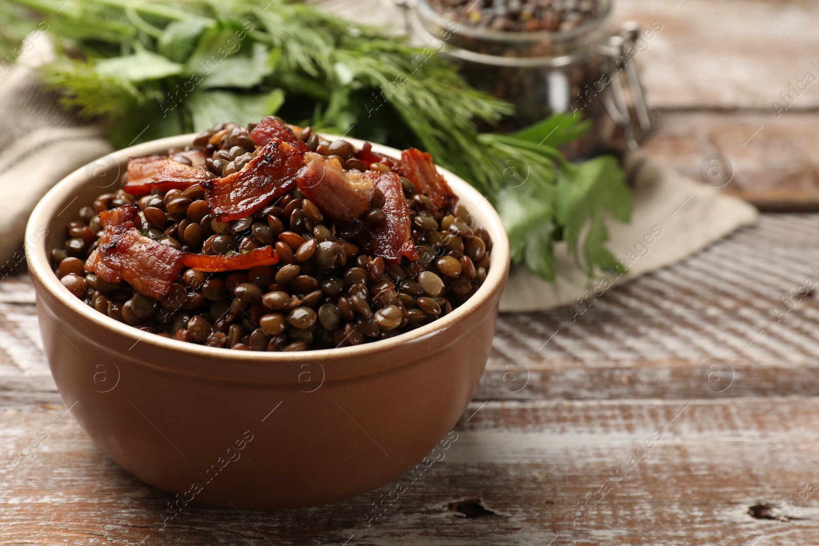 Photo of Delicious lentils with bacon in bowl on wooden table, closeup. Space for text