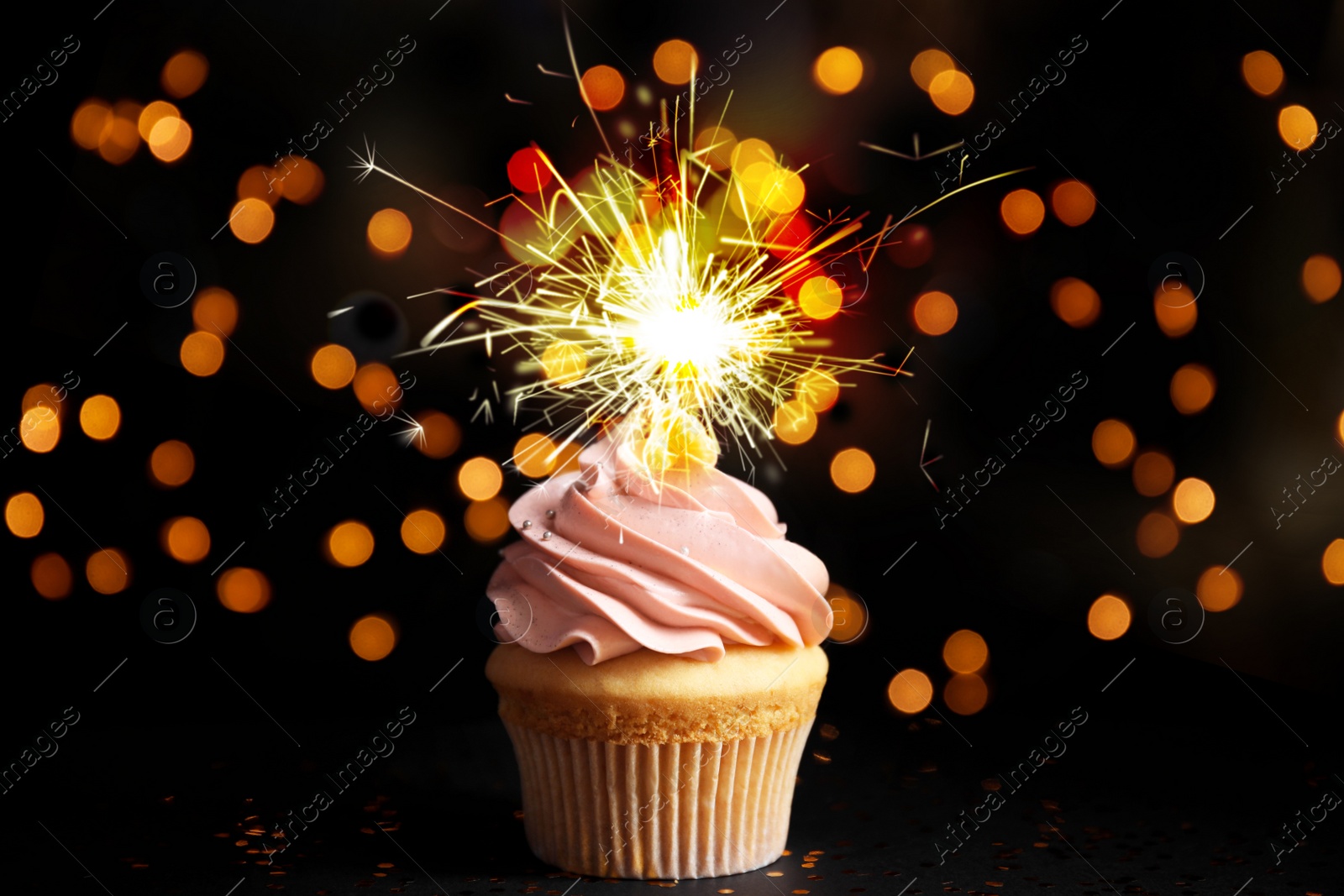 Image of Delicious birthday cupcake with sparkler on black table against blurred lights