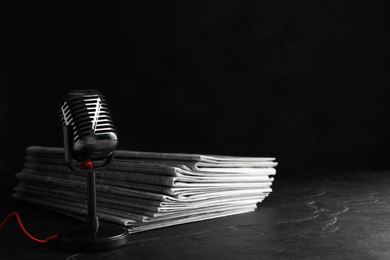 Photo of Newspapers and vintage microphone on dark stone table. Journalist's work