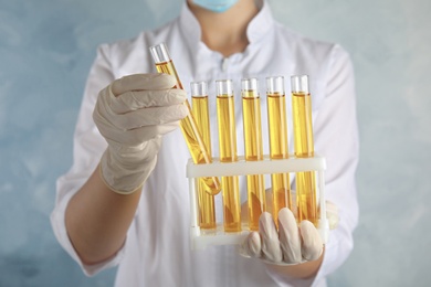 Photo of Doctor holding test tubes with urine samples for analysis on light blue background, closeup