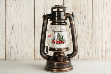 Beautiful snow globe in vintage lantern on light wooden table