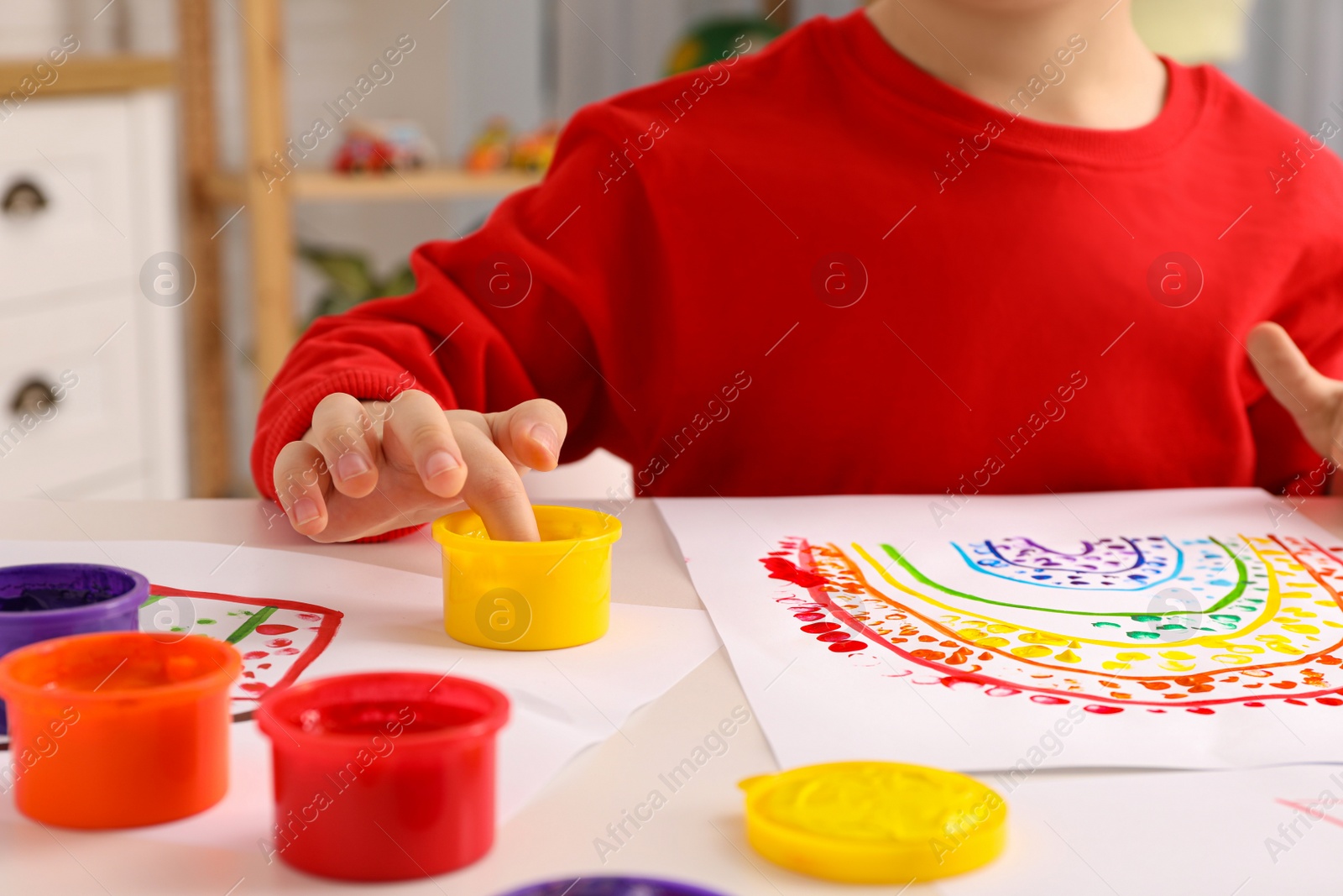 Photo of Little boy painting with finger at white table indoors, closeup