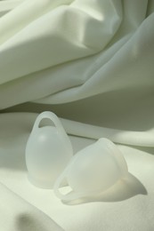 Photo of Menstrual cups on light fabric. Reusable female hygiene product
