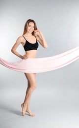 Photo of Young slim woman covering her body with fabric on light background. Space for text