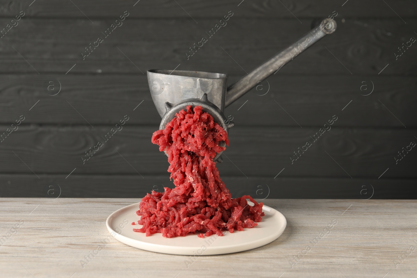 Photo of Metal meat grinder with beef mince on light wooden table