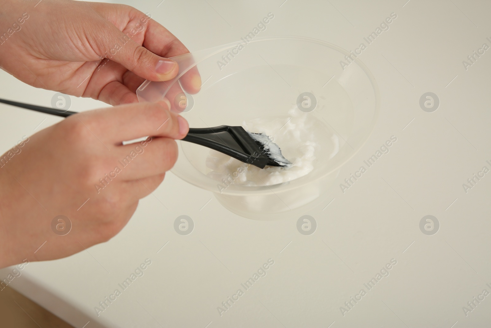 Photo of Woman preparing hair dye in bowl at white table, closeup