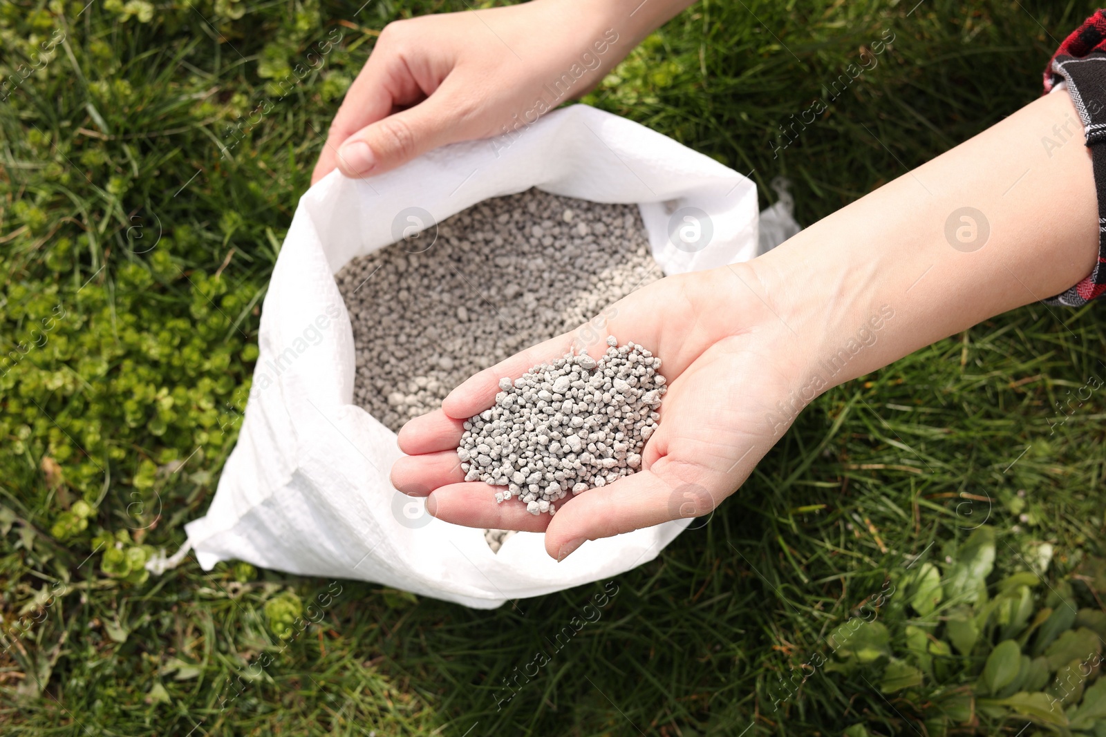 Photo of Woman with fertilizer on green grass outdoors, top view