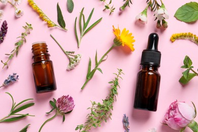 Bottles of essential oils, different herbs and flowers on pink background, flat lay