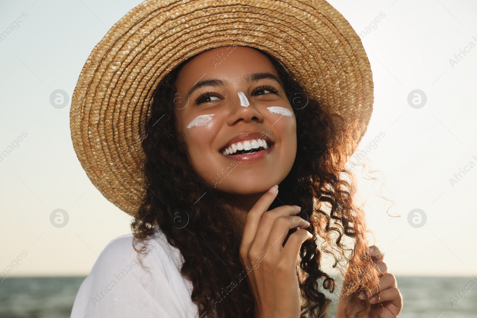 Photo of Happy African American woman with sun protection cream on face near sea