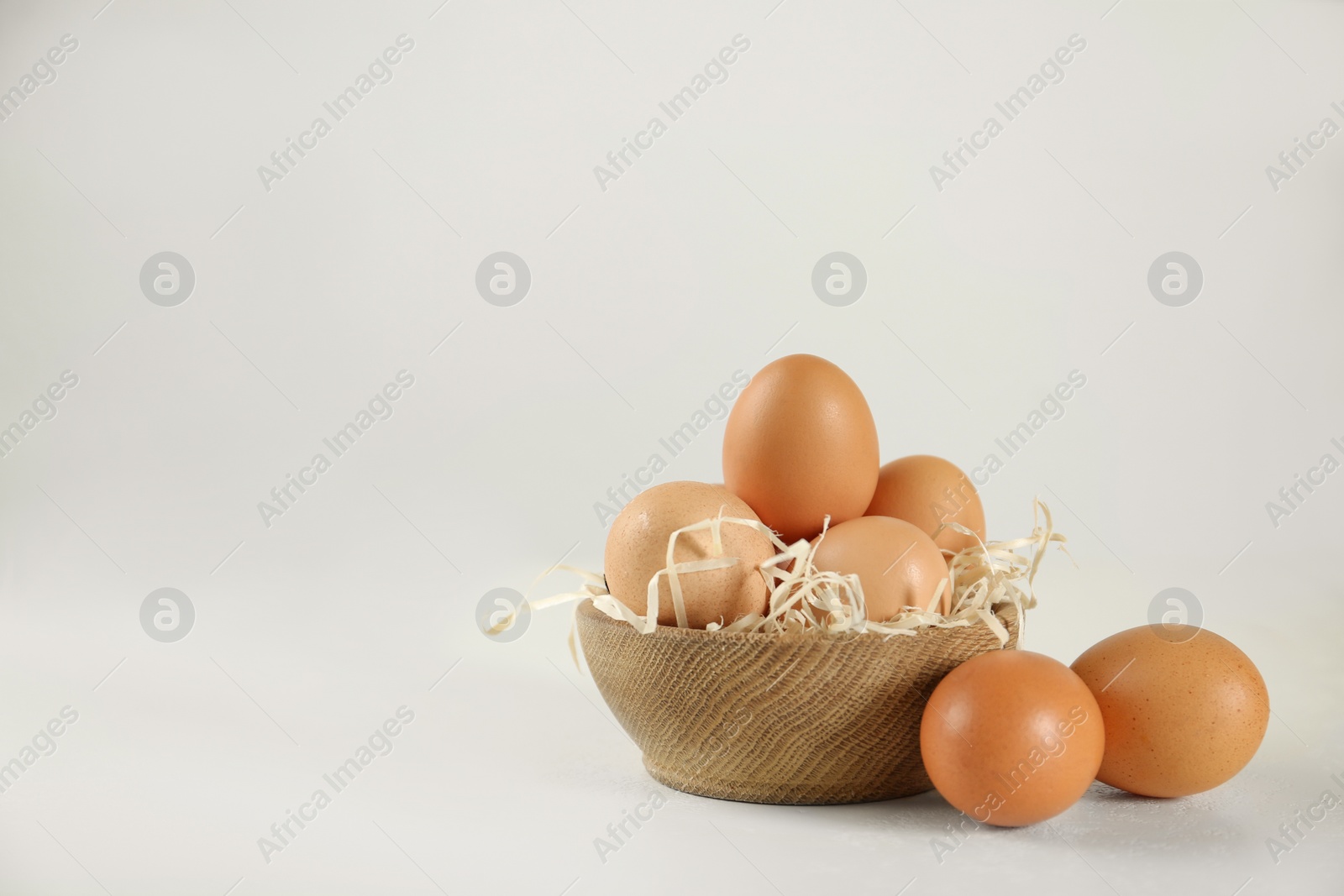 Photo of Raw chicken eggs and decorative straw on white table. Space for text