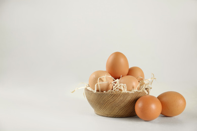 Raw chicken eggs and decorative straw on white table. Space for text