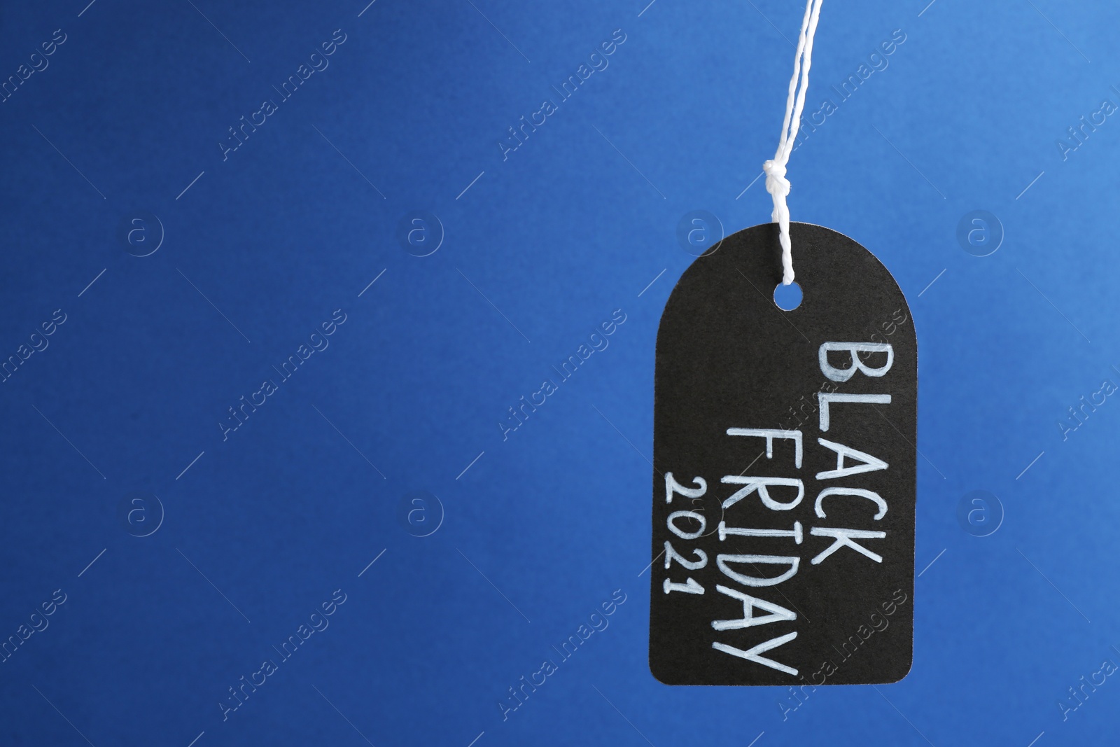 Photo of Tag with words BLACK FRIDAY 2021 hanging on blue background. Space for text