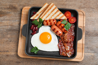 Delicious breakfast with heart shaped fried egg and  sausages on wooden table, top view